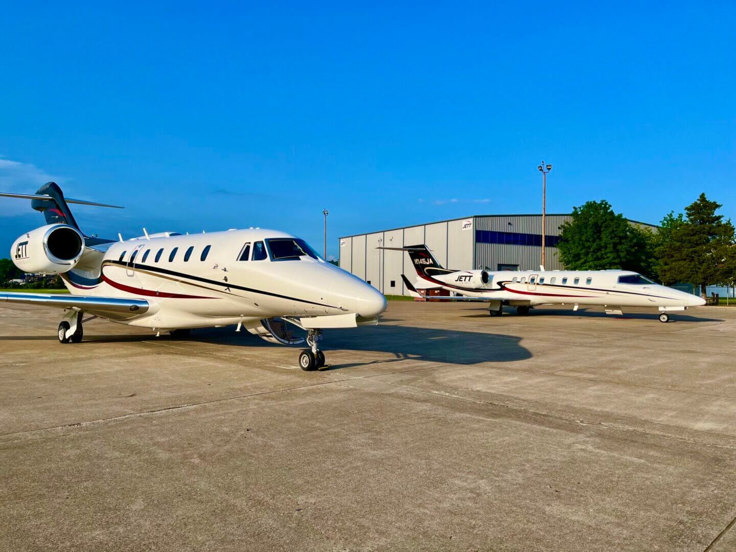 Two private jets parked on an airport tarmac under a clear blue sky.