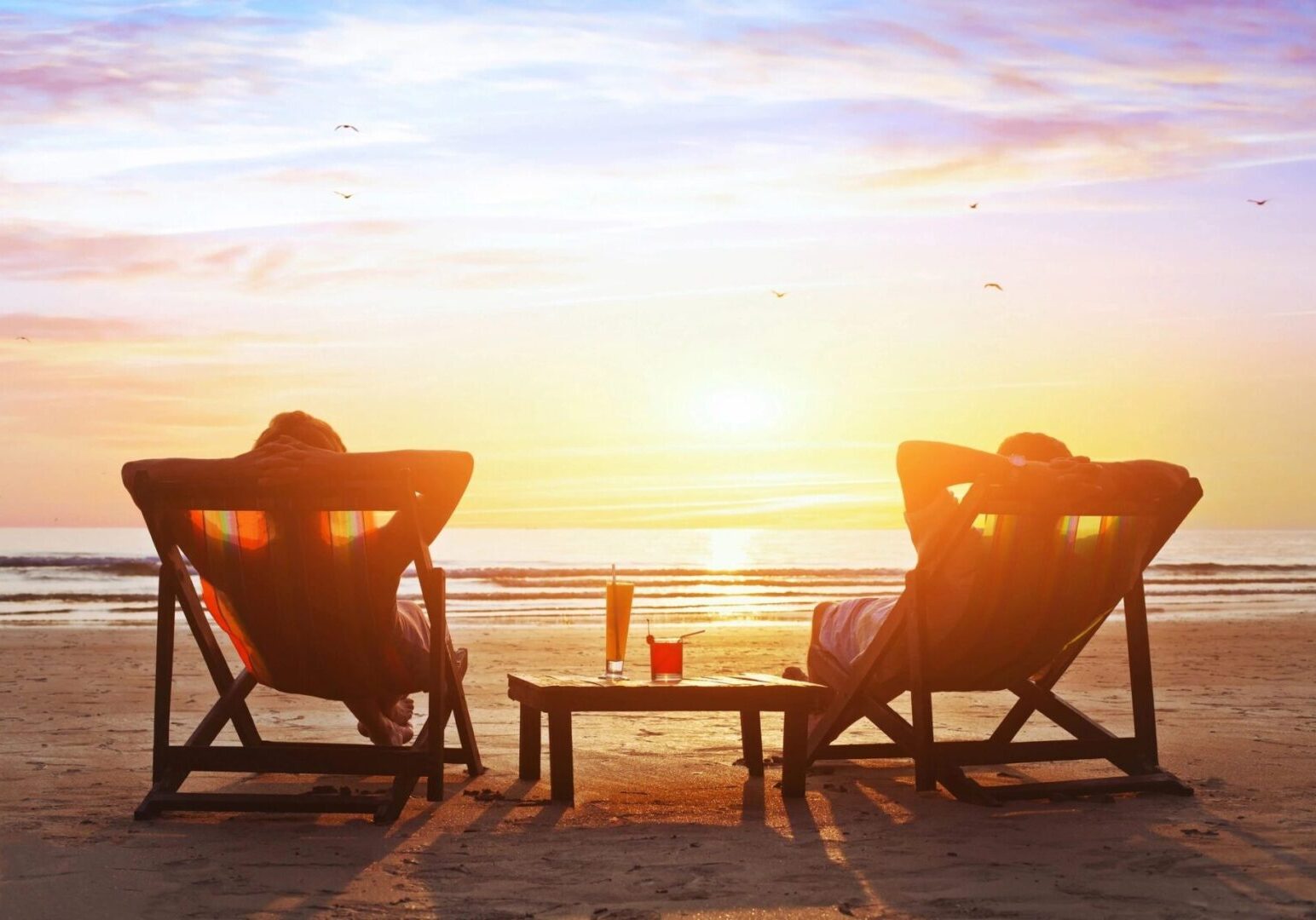 Two people relaxing on beach chairs watching the sunset over the ocean.